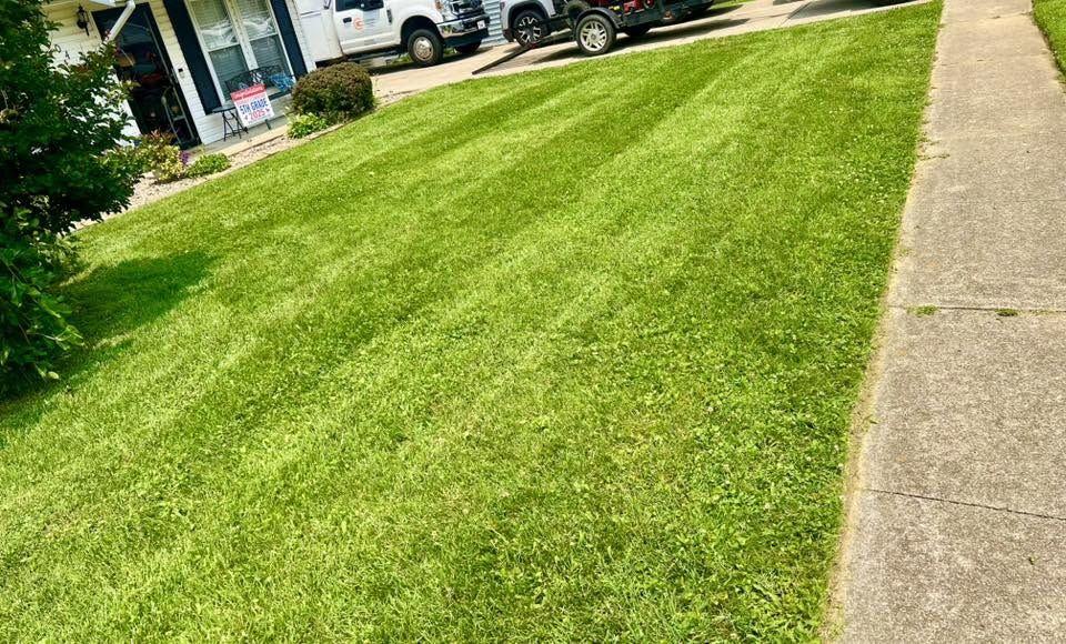 A front lawn with faint mowing stripes and the service truck sitting in the driveway.