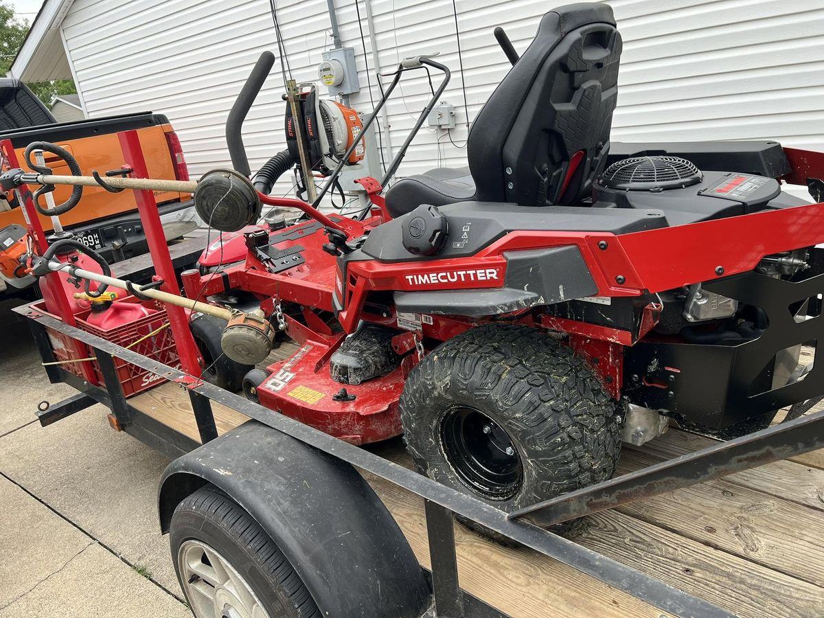 The red Toro TimeCutter loaded on the open trailer with the Stihl trimmers racked alongside it.